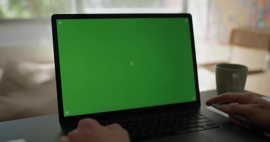 Laptop on the table while a person holds a remote control next to a cup of coffee