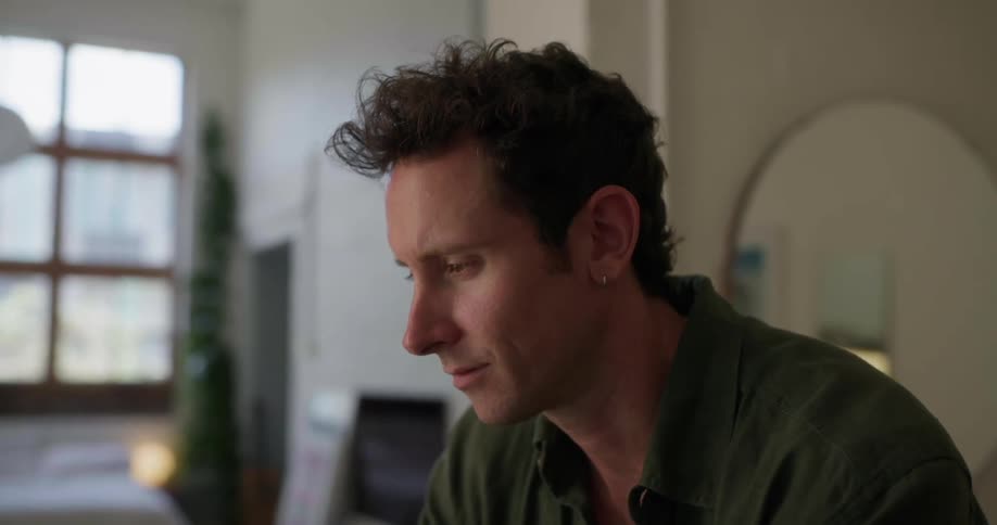 The face of a man looking forward who begins to smile and then places his hands on his chin and becomes thoughtful