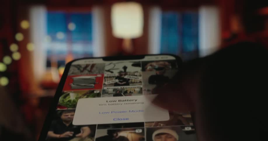 A person is scrolling through images on a smartphone likely on a social media application in a dimly lit room