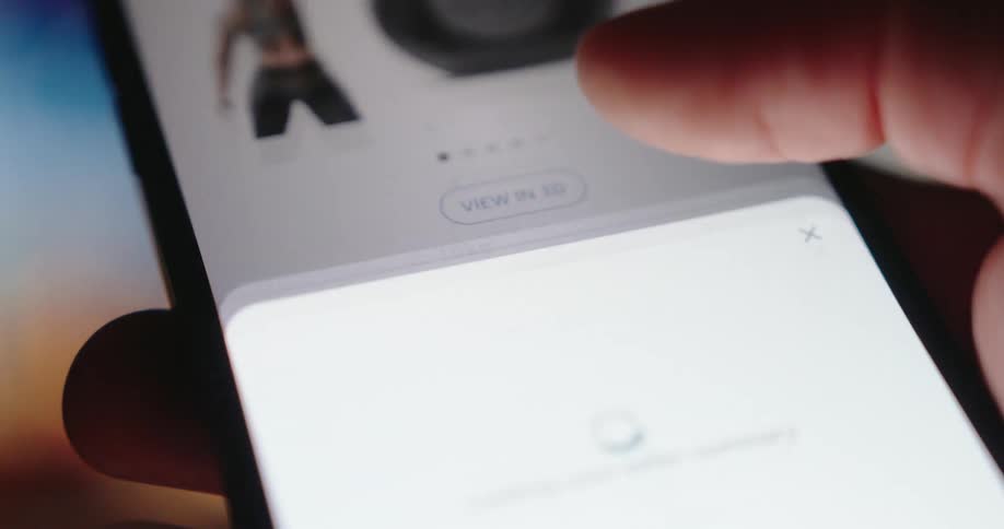 A finger presses the buy now button on a smartphone screen initiating an online purchase