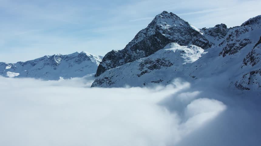 Snowcovered mountain peaks rise above a thick layer of clouds
