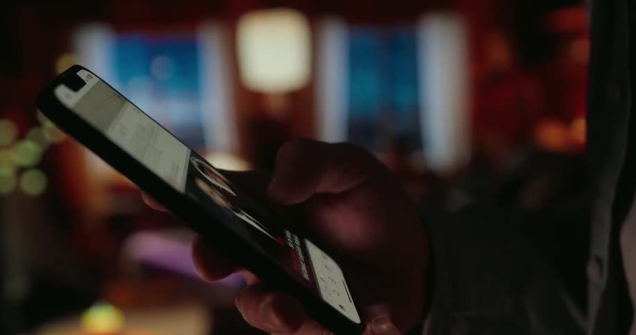 Person standing indoors scrolls on their smartphone