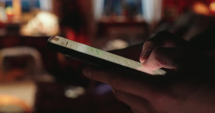 A person is texting on a smartphone in a dimly lit room with a warm cozy ambiance