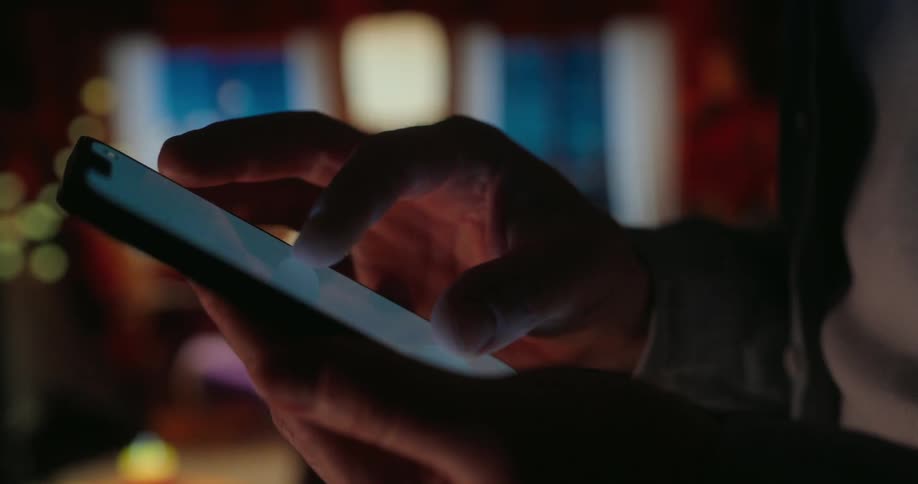 A person is using a smartphone in a dimly lit room with a warm cozy ambiance