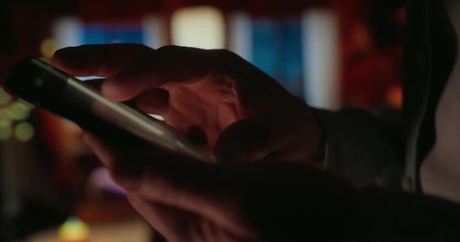 A person is using a smartphone in a dimly lit room with a warm cozy ambiance