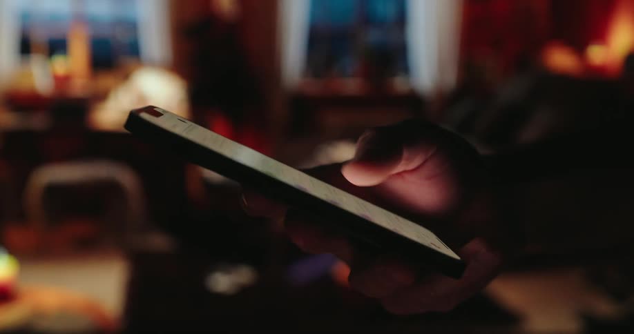 Man scrolls on a smartphone while it storms outside at night