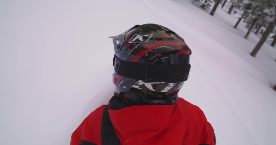 Someone wearing a helmet and red jacket snowmobiling through a snowy landscape