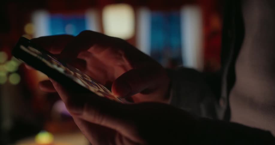 A person is using a smartphone in a dimly lit room with a warm cozy ambiance