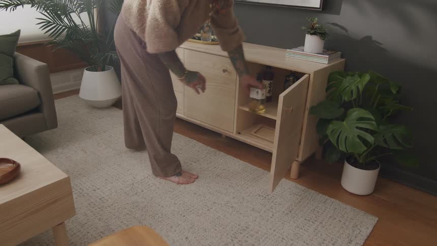 A person opening the small door of a wooden rack that is leaning against a wall in a living room