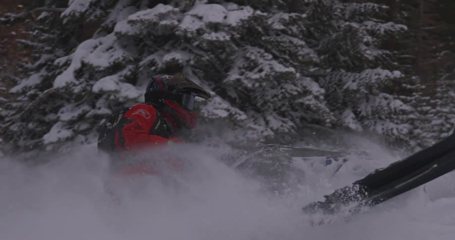 A person wearing a helmet and red clothes and is using a ski fashion to ride in the snow and do maneuvers throwing snow to the sides