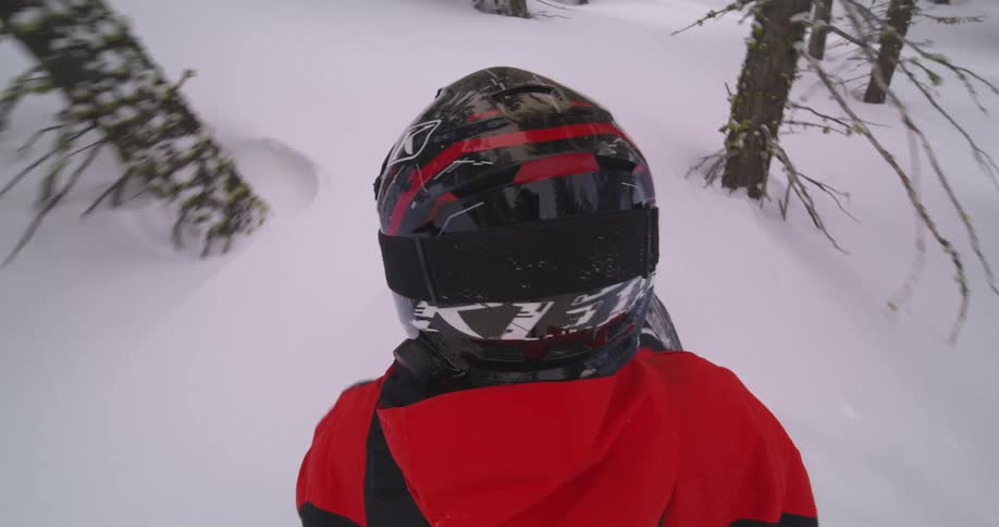 Person in protective helmet riding snowmobile through a snowy forest