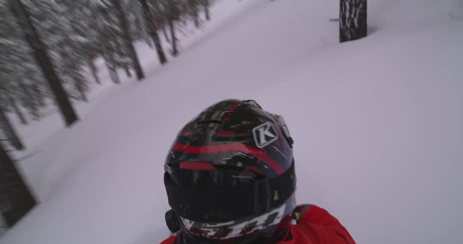 Person in helmet traveling through snowy mountain and forest on snowmobile