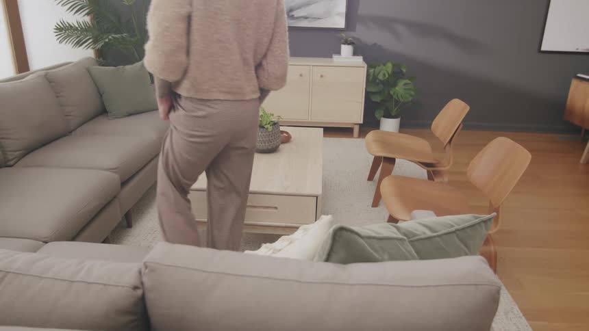Man walks across the living room area and prepares to sit on the couch