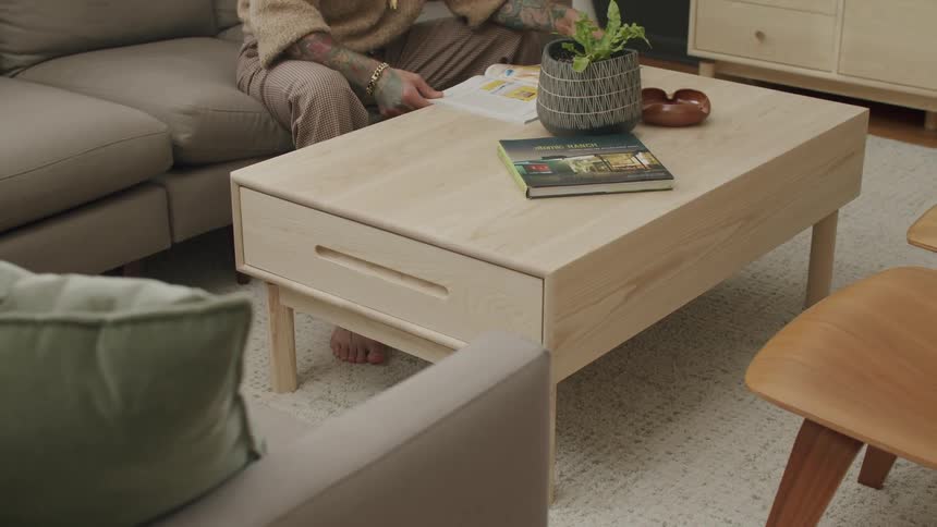 A wooden rack in the center of a living room where there is a person sitting on a gray sofa next to it