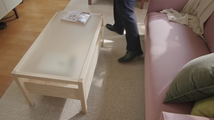 A person stands up from a pink sofa while holding a drink next to a wooden coffee table