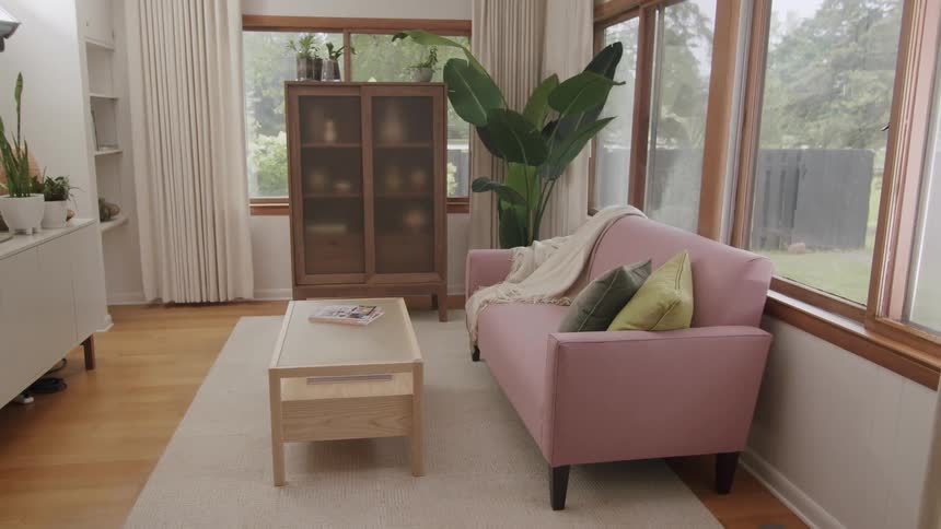A living room with a pink sofa with pillows and some windows on the walls