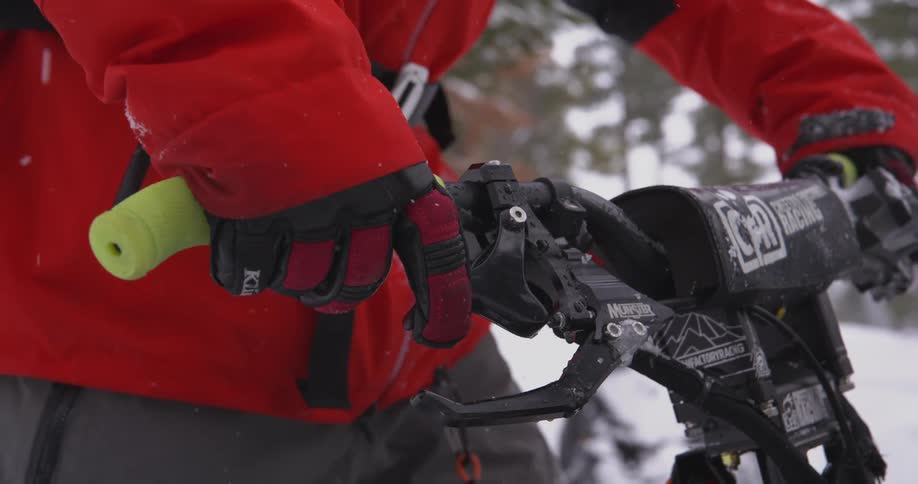 Person wearing red winter clothing holding the handlebars of a snowmobile
