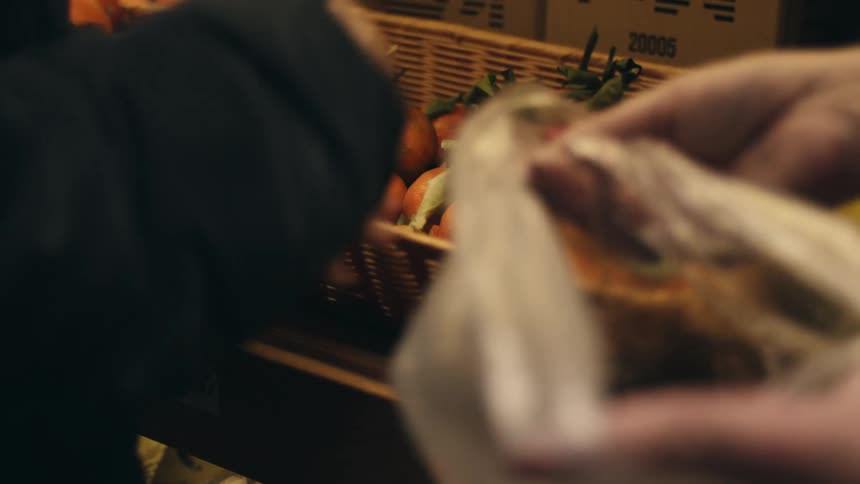 Two people are selecting oranges from a basket with one person holding a plastic bag