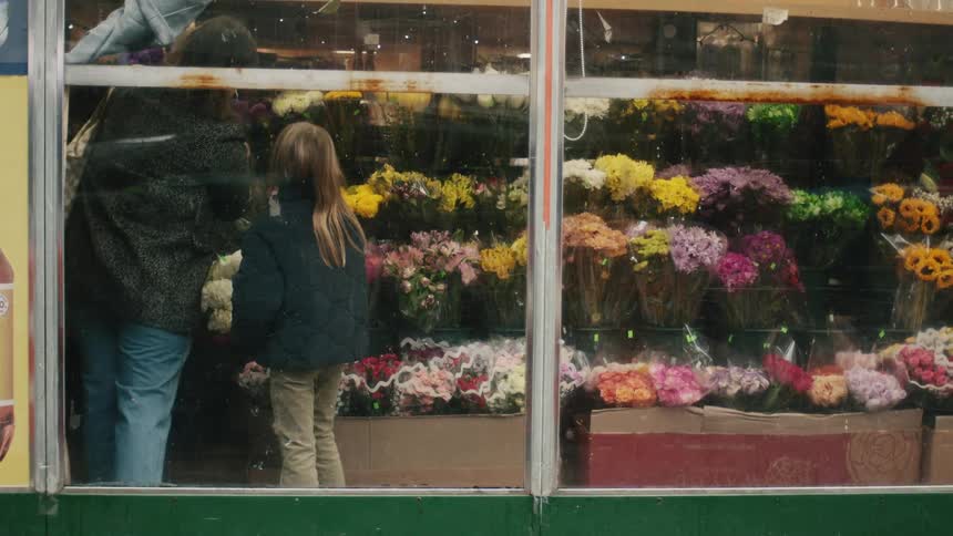 Mother and daughter seen shopping for flower bouquets through a store window