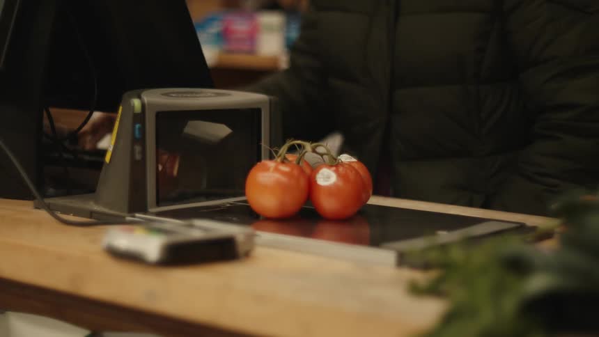 A person placing four tomatoes on top of a supermarket checkout scale