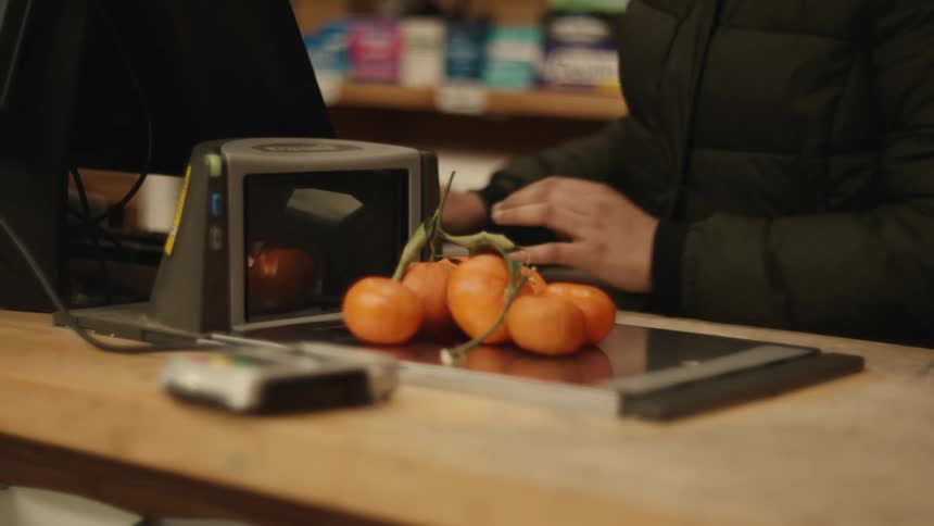 Grocery shop clerk placing some fruit on the weighing scale at check out