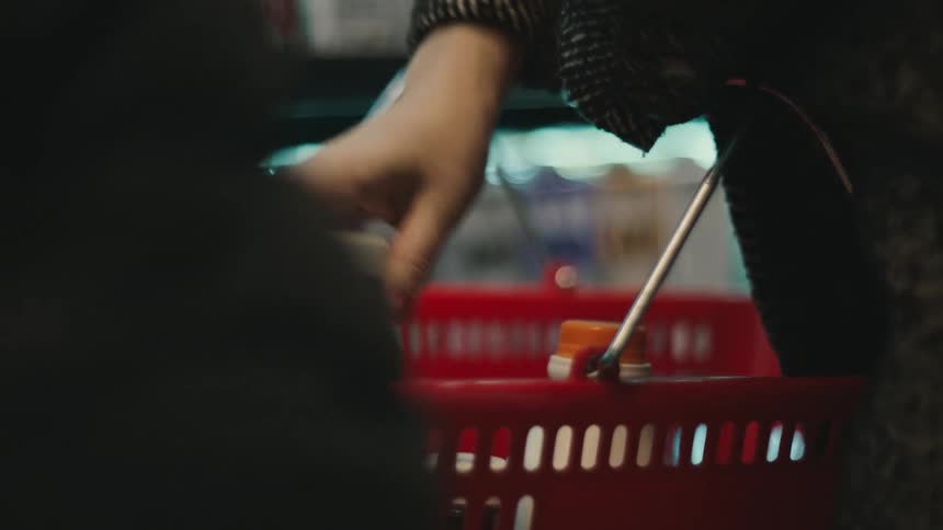 A person places bottles into a red shopping basket in a store