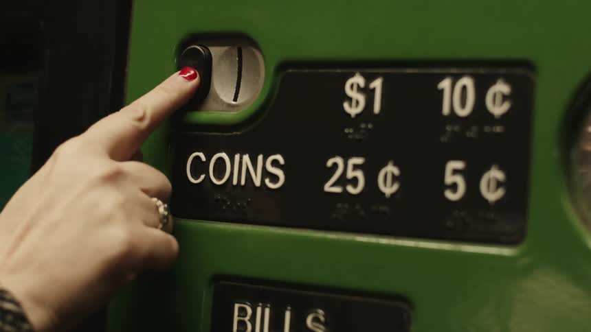 A persons hand putting a coin into a machine and then pressing a black button
