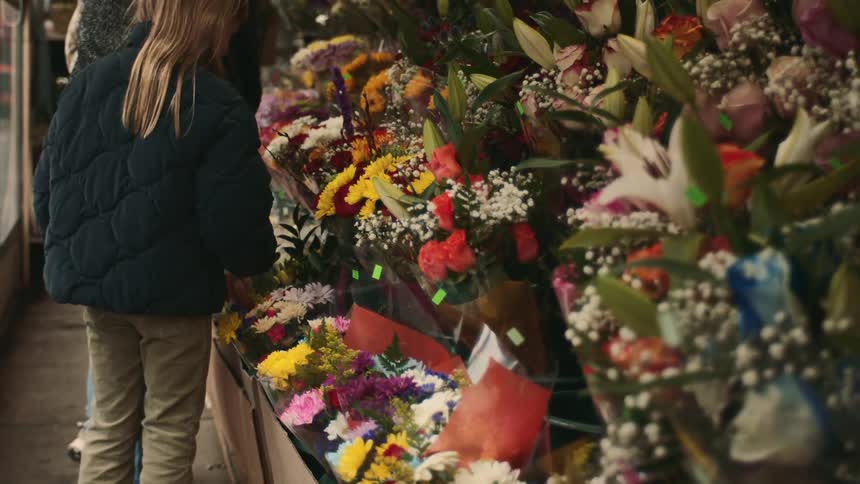 An adult and a little girl looking at a shelf full of colorful flowers on display and picking one of them