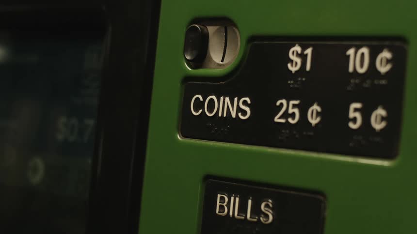 A persons hand putting a coin into a machine with white texts