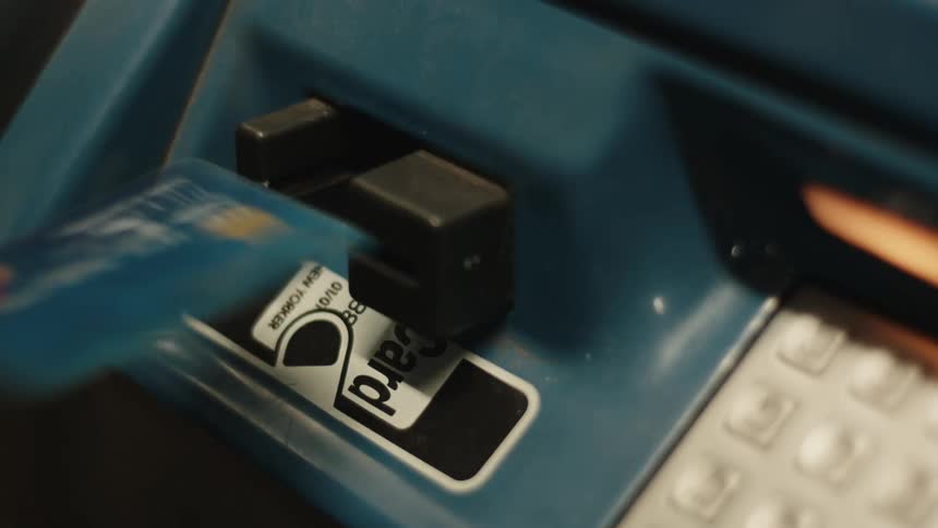 A hand is inserting a credit or debit card into a blue card reader machine which has a keypad visible to the right