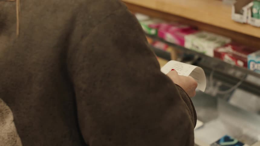 A person with a white paper purchase receipt in his hand with red nails