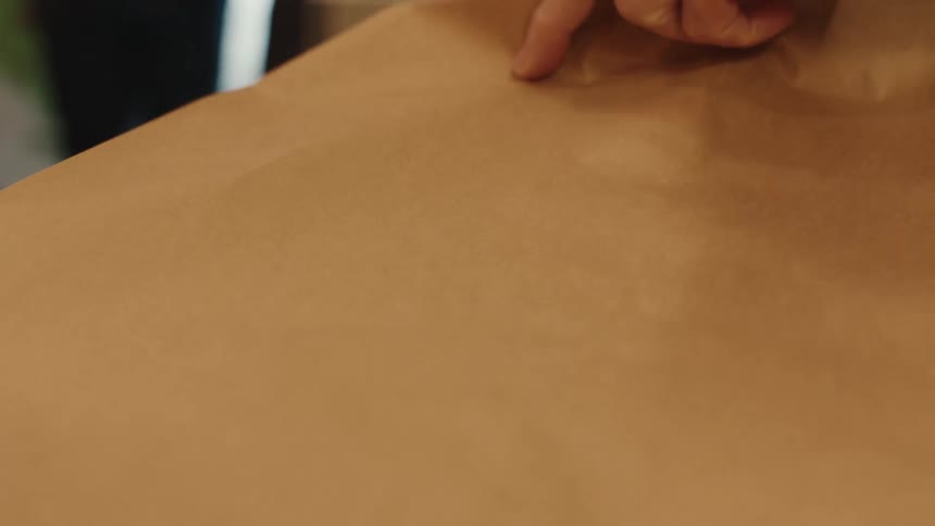 A persons hand placing a photo frame in a cardboard bag that is on top of a shopping cashiers table