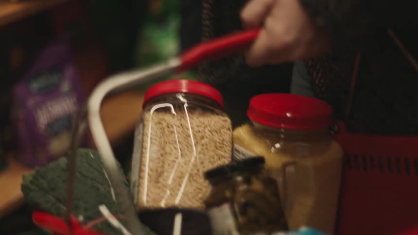 A person putting some grocery items into a red shopping basket
