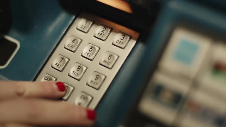 A hand with redpainted nails is pressing numbers on the keypad of an atm