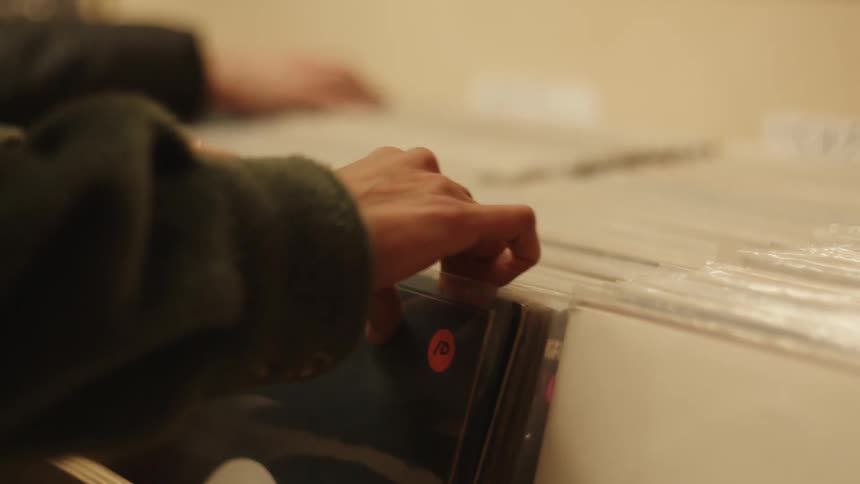 A person is browsing through a collection of vinyl records with colorful price stickers