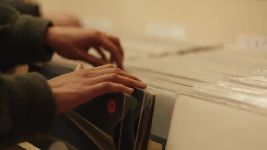 Person flips through vinyl records arranged in a box with colorful price tags