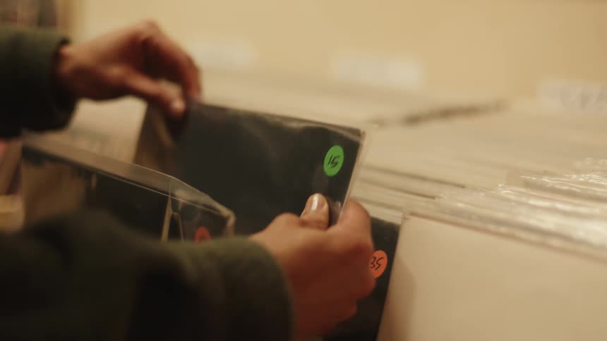 A person is browsing through a collection of vinyl records with colorful price stickers