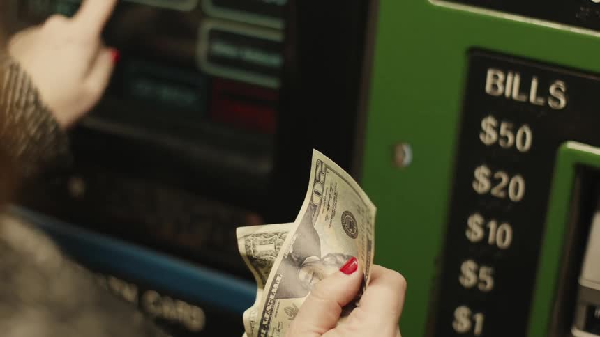 Fingers typing on an atm screen while the other hand holds banknotes