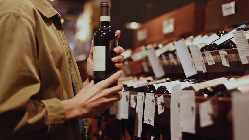 Person holds a bottle of wine while looking at the shelf in a liquor store