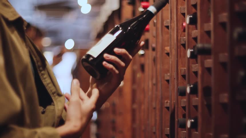 Person places and removes a bottle of wine from a cellar with wooden shelves filled with bottles