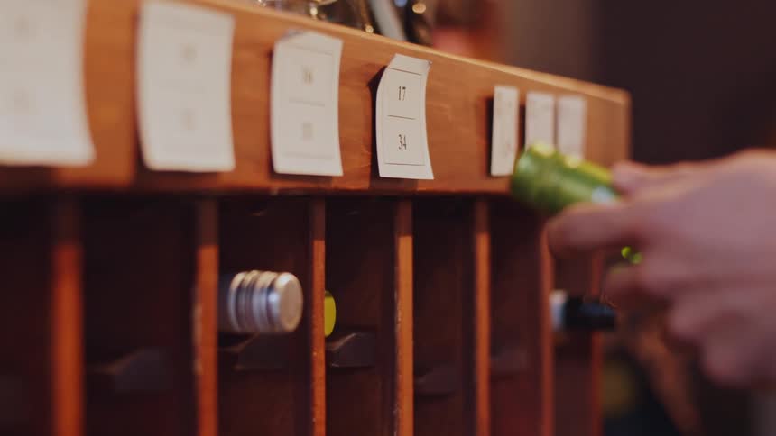 Pair of hands picking up and returning a bottle of wine on a wooden shelf
