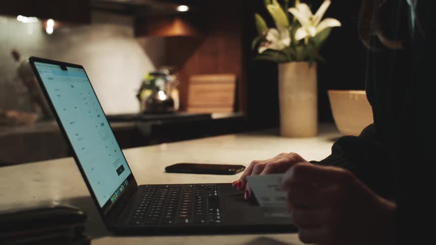 Person holding a credit card in front of a laptop