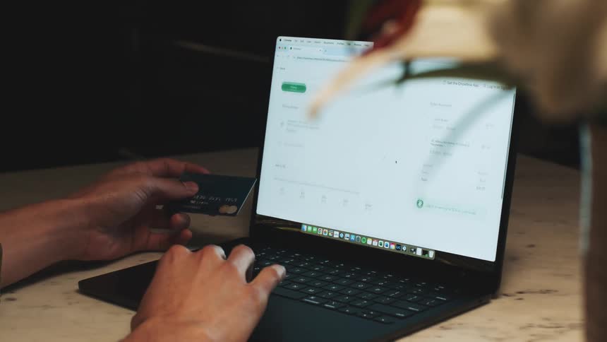 A man is using a credit card to pay on his laptop