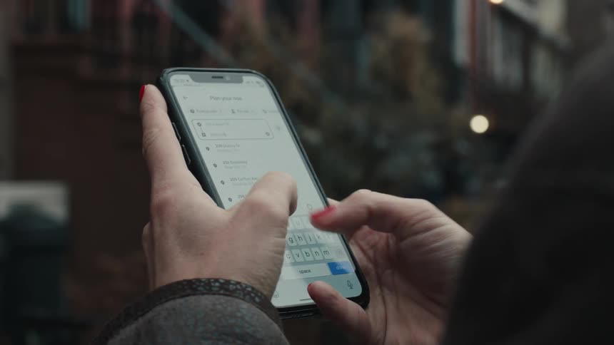 A person holds a smartphone interacting with the screen with buildings and lights in the background