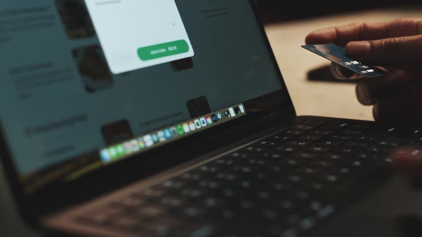 Hand holding a credit card facing an open laptop screen
