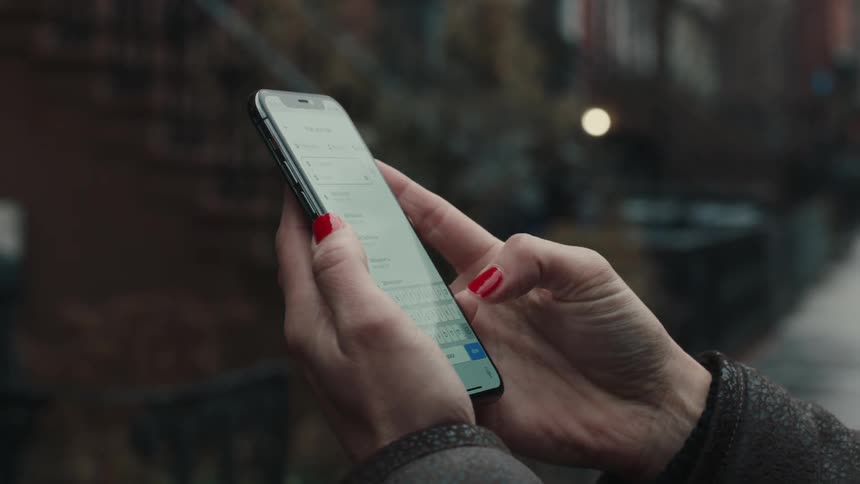 A woman is typing on her cell phone while standing on the sidewalk
