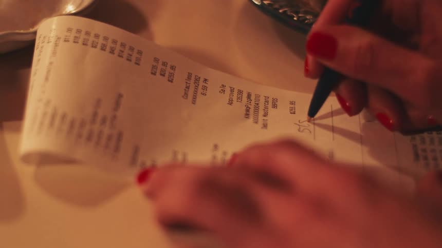 Person signs a receipt on the table with a blue pen