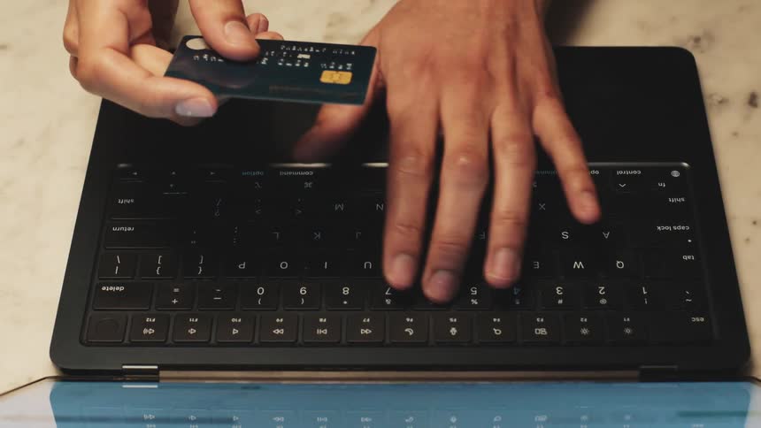 Hands holding a credit card above the keyboard of an open laptop on a marble table