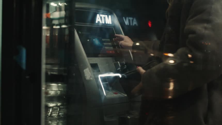 A person is using an atm machine at night with the screen and keypad visible and the person holding a wallet or card near the card slot