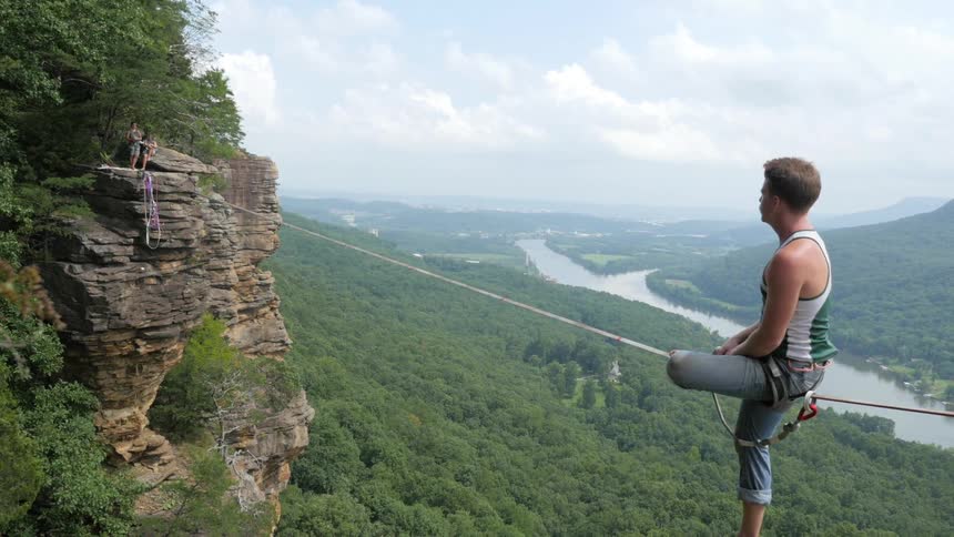Man sits on a line between two cliffs on a cloudy day